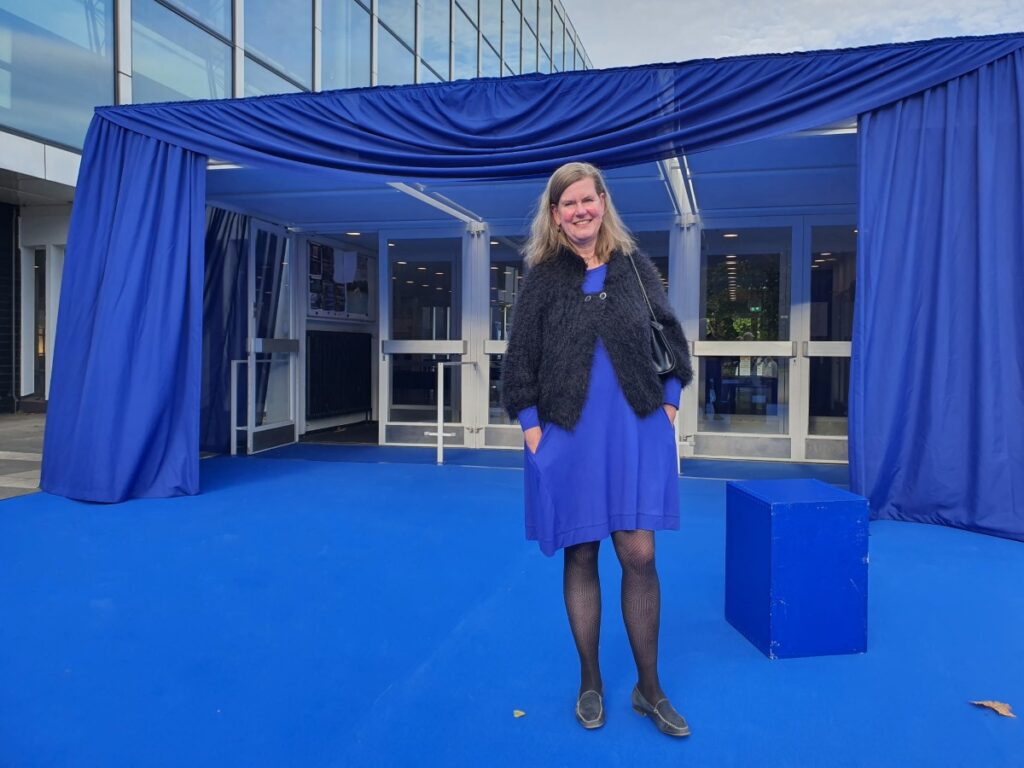Monika Wyrobisch im blauen Kleid vor dem blau gestalteten Eingang des Musiktheaters im Revier in Gelsenkirchen.